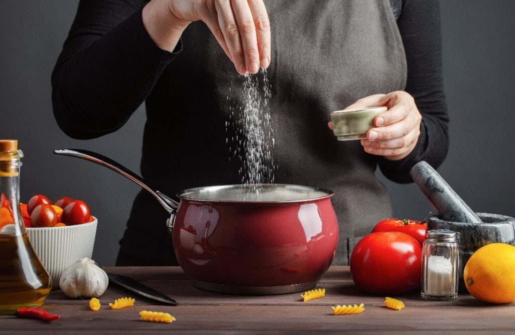 Der Koch bereitet Spaghetti und Nudeln, Salzwasser, vor einem dunklen Hintergrund, das Konzept des Kochens. Frau Salzwasser vor dem Kochen von Nudeln Fusilli